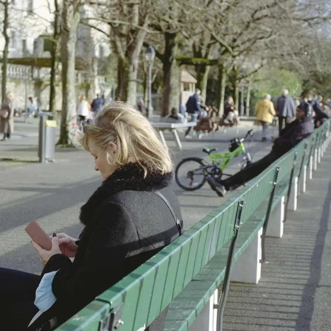 Femme lisant sur un long banc vert au soleil d’hiver