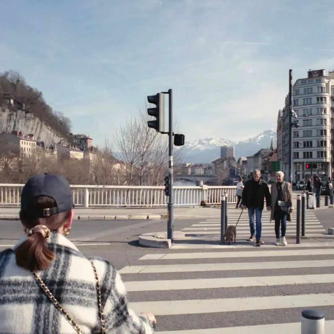 Passants sur un pont à Grenoble, montagnes enneigées au fond